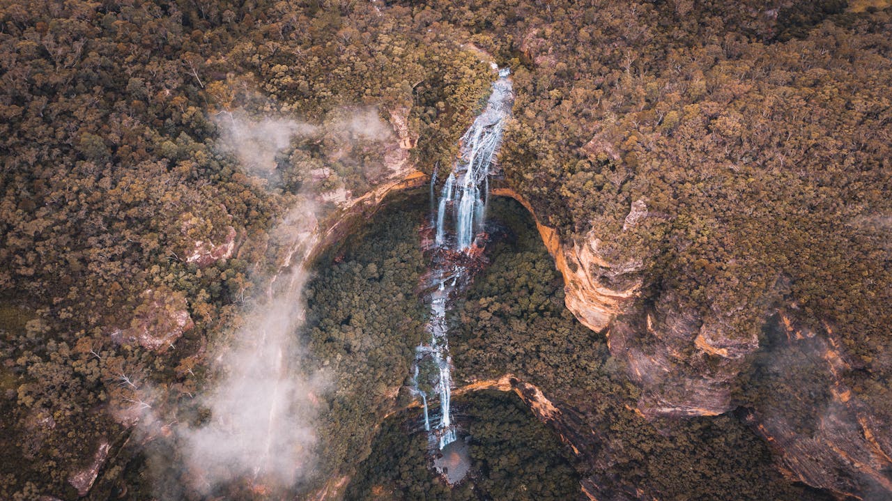 services-img-01 Discover the stunning aerial view of a waterfall cascading through the lush forests of Australias Blue Mountains.